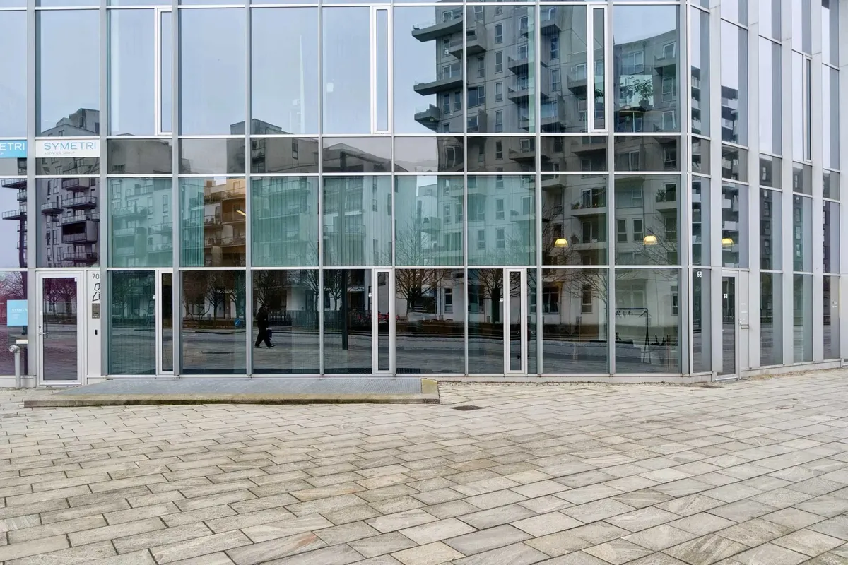 Prisbelønnet ejendom med glasfasade og enkeltperson går i forgrunden foran bygningen med flere etager og store vinduer