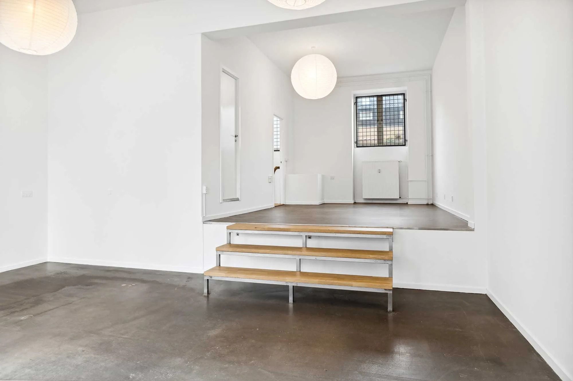 Moderne, lyse lokaler med højloft og trætrapper, der fører op til et højere niveau med vinduer og radiatorer