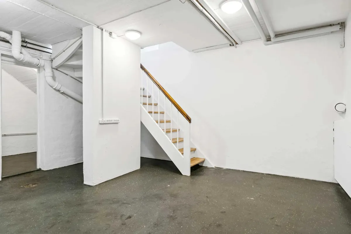 Et tomt lokale med hvide vægge og gulv samt et tretrins trappeløb mod væggen og røret på loftet.