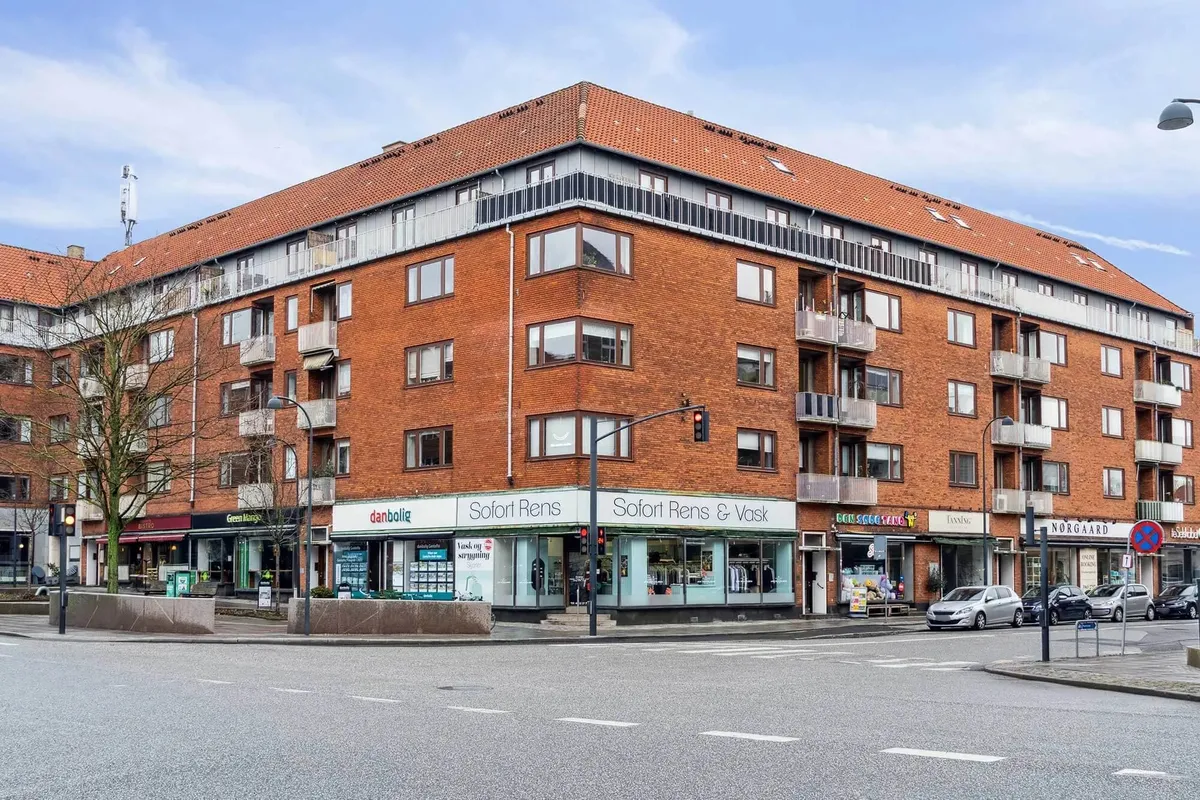 Rødstøjen bygning med mange lejede butikker og parkeringspladser på Baunegårdsvej 3A i Gentofte