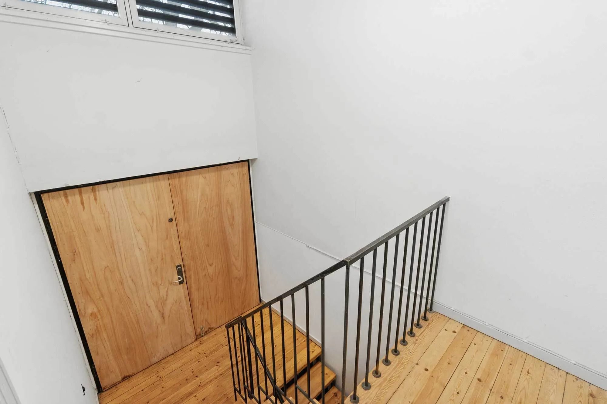 Trætrapper i hjørne med håndtag og trin, der fører op til et lukket trædør og et hvidt vægpanel