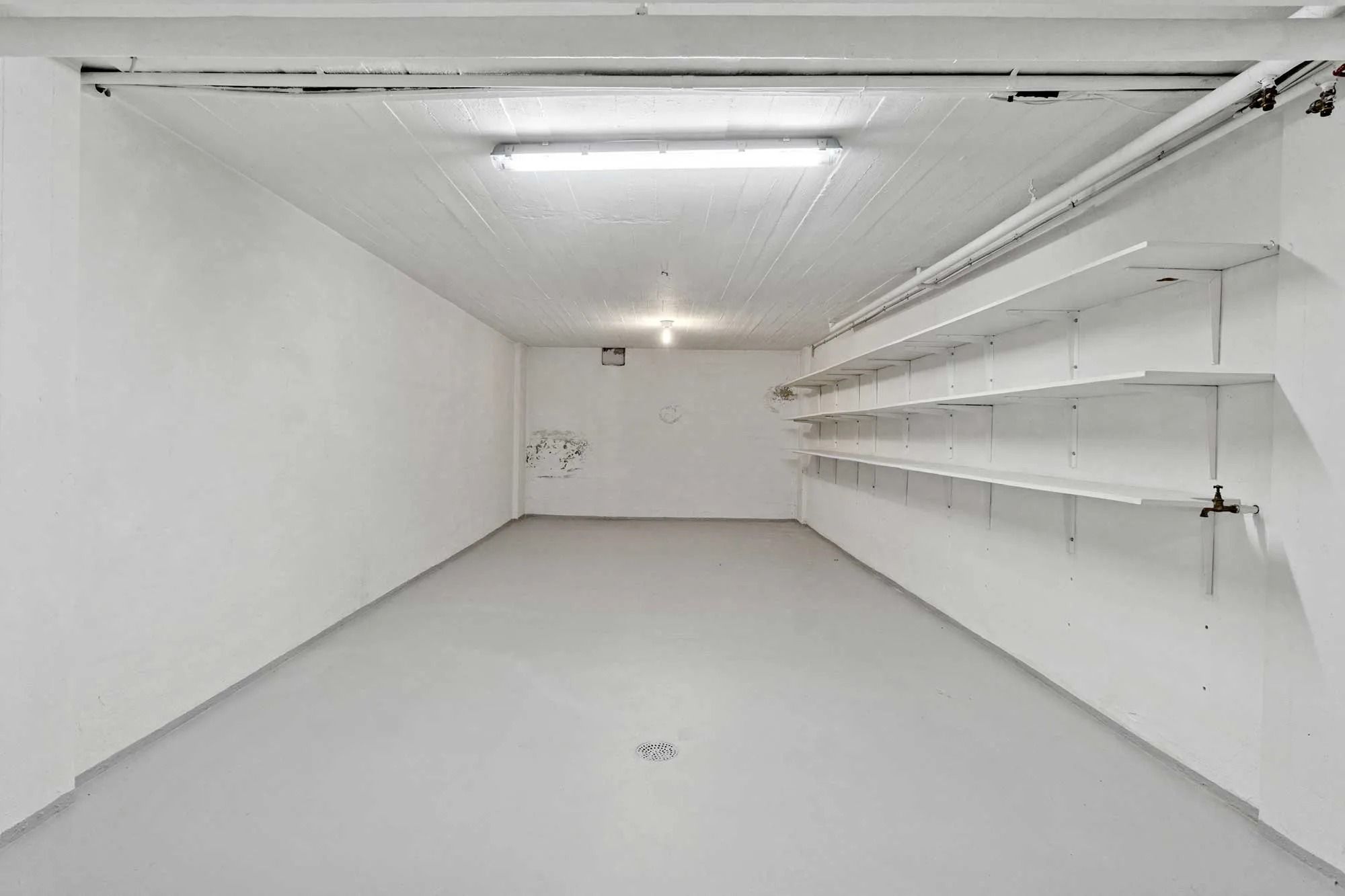 Pop-up butik med hvid maling og lyst gulv. Der er et loft med en hvid bjælke og to lyse. Væggene er hvide med to hvide