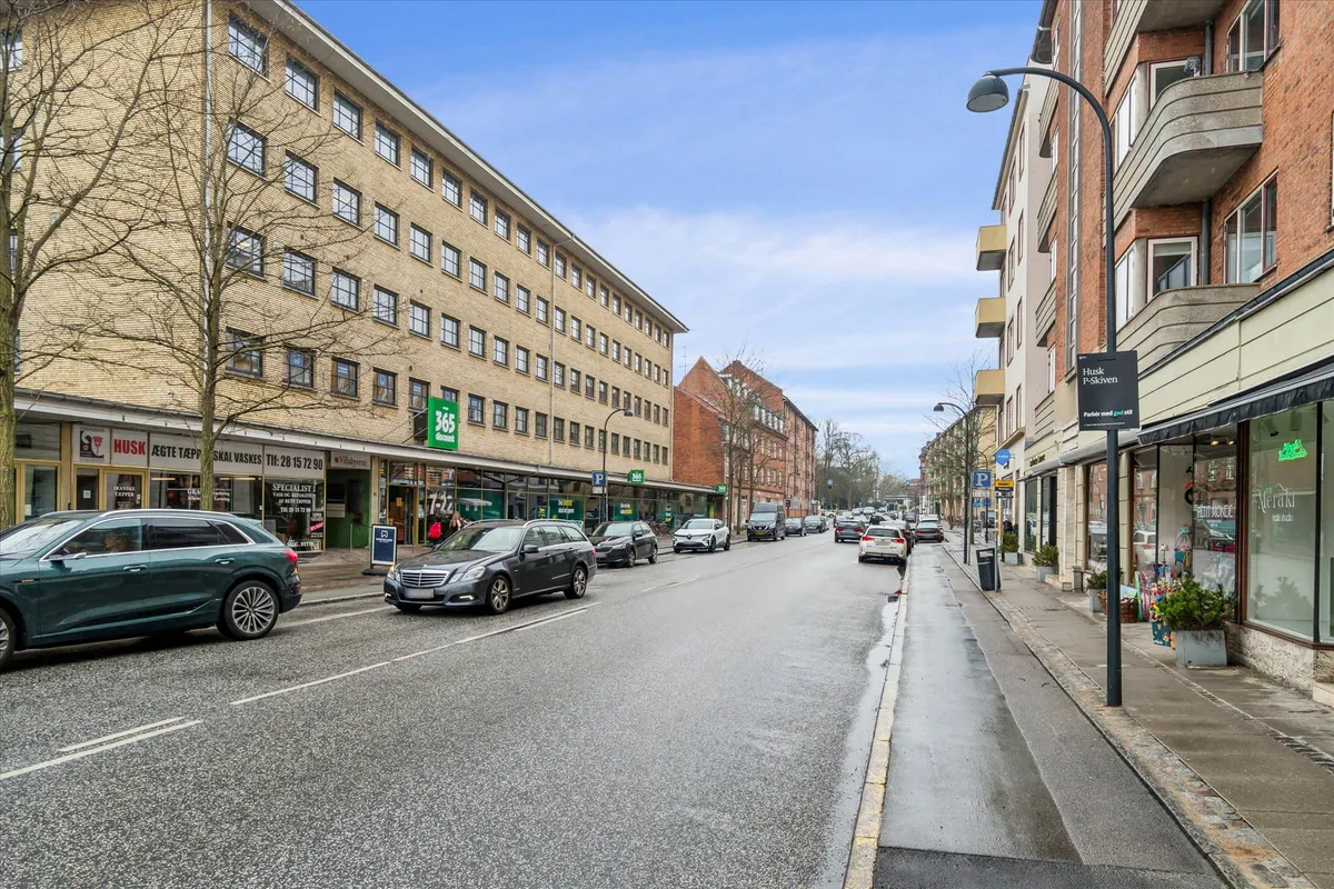 To biler parkeret langs en tosporet gade med kontorer, butikker og beboelsesejendomme langs vejen