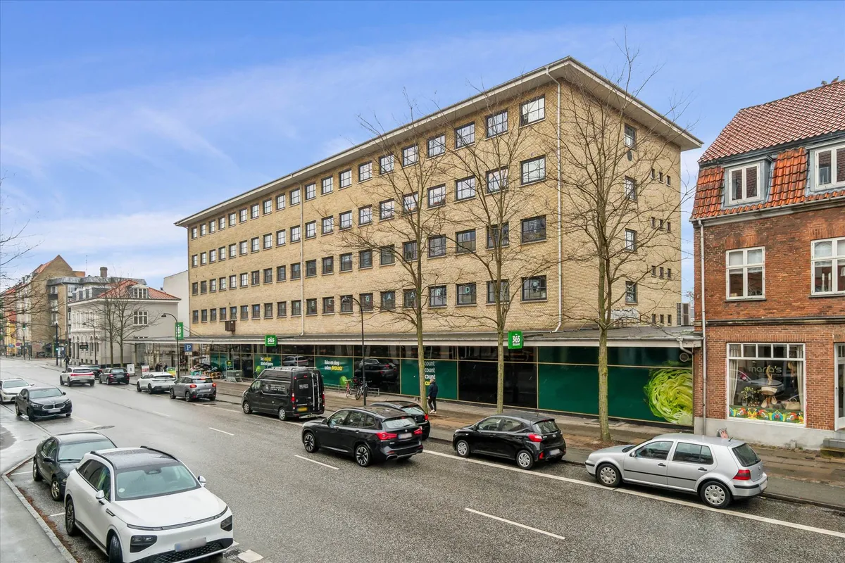 Flere biler parkeret på hver side af en bred gade med butikker og gafvogne på forgrunden