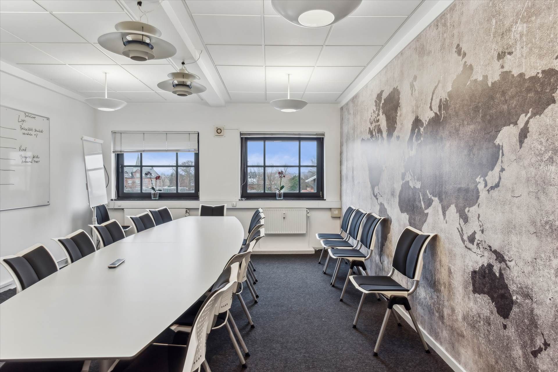 Kontorrum med bord og stole og tavle med notitser og plante på vindueskarmen