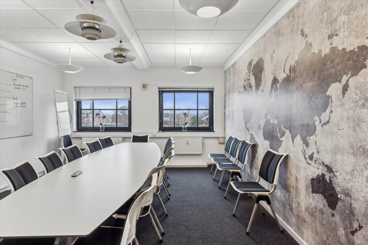 Kontorrum med bord og stole og tavle med notitser og plante på vindueskarmen