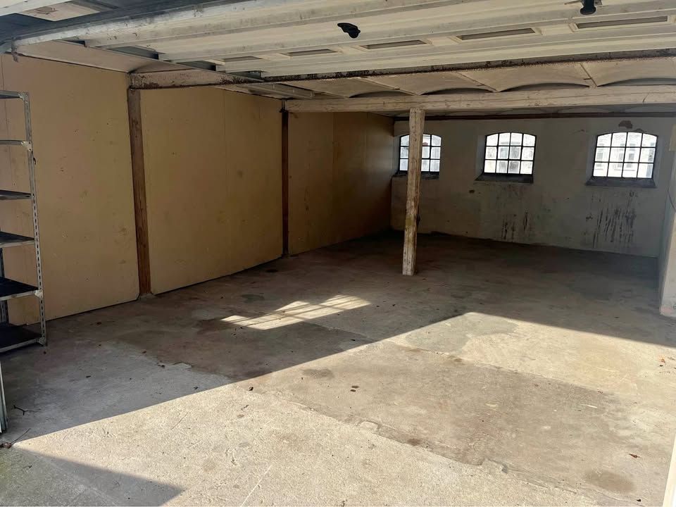 Garage med cementgulv og tre vinduer på den modsatte side samt en metallskabs på venstre side