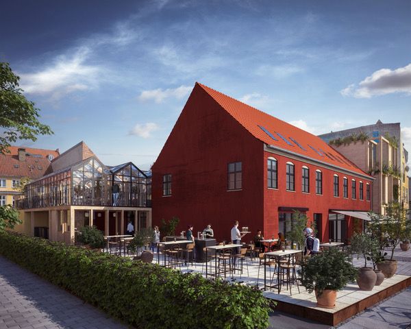 En stor rød bygning med solpaneler på taget og en rummelig gårdhave med borde og stole og grønne planter