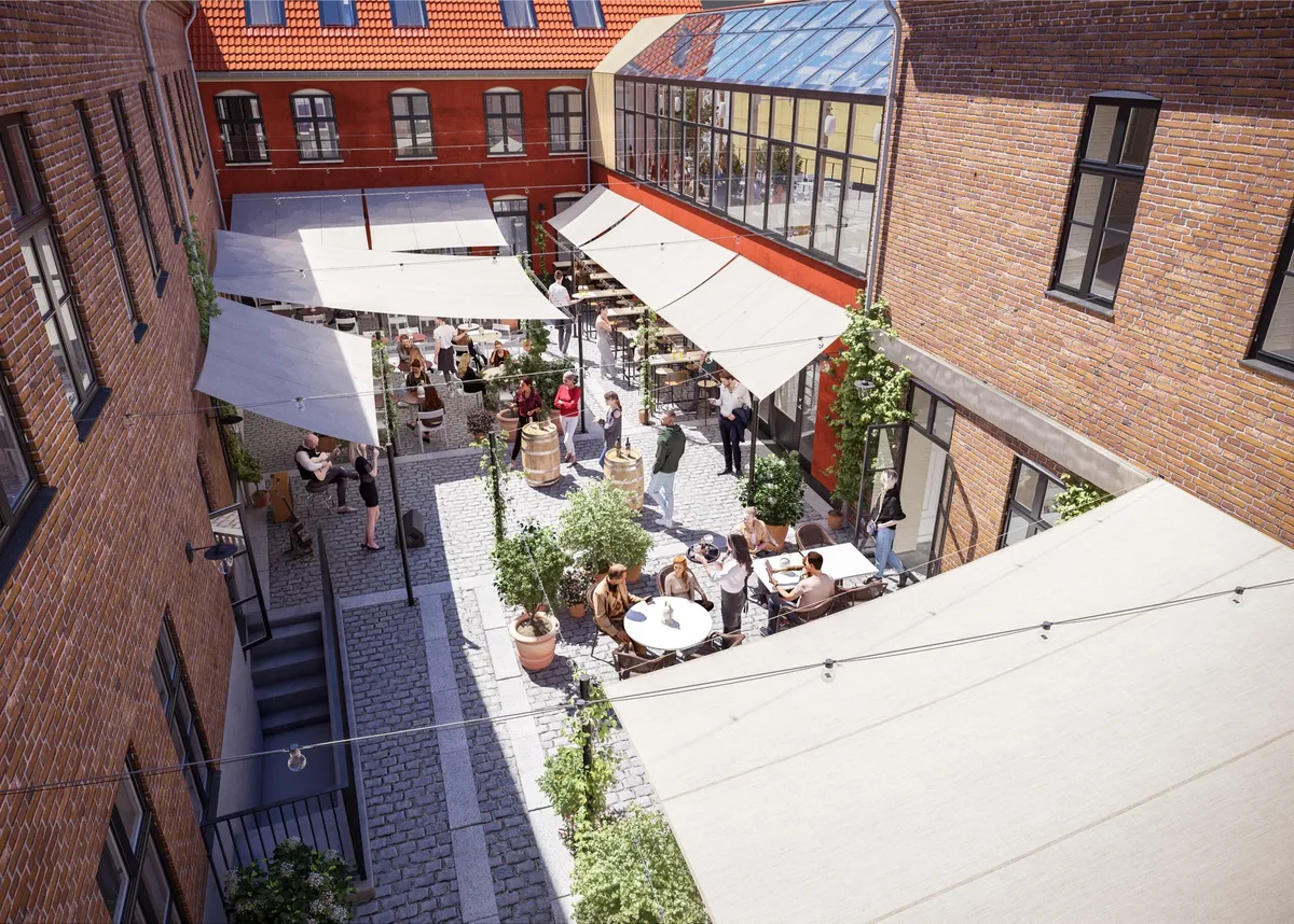 Mange mennesker nyder en dag i sommersol på et caféområde med bord og bænke, træffade vin og parasoller