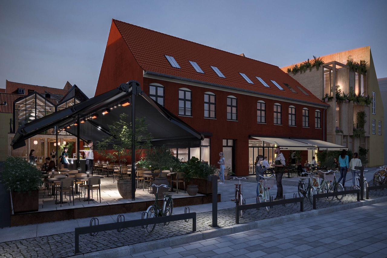 Bygning med rødt tag, terrasse med bord og stole og folk, der går og cykler på gågaden