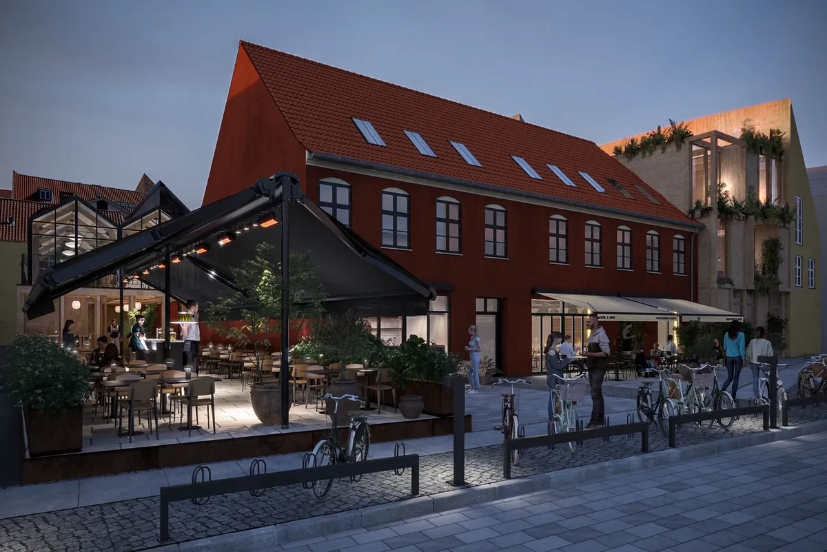 Bygning med rødt tag, terrasse med bord og stole og folk, der går og cykler på gågaden