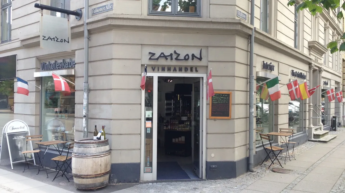 Vinbar Zaizon med stolpe og træfat udenfor og flere vinduer og flag med forskellige lande på facaden