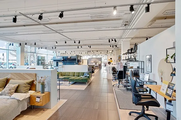 Indvendigt i et stort butikslejemål med sofaer, seng, skriveborde, stole, smykker, blomster og vægmaleri