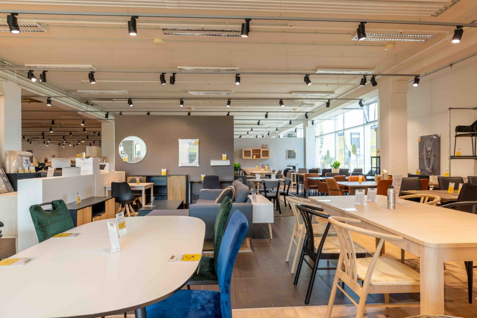 Lyst og rummeligt møbelforretningslejemål med bord, stole og sofaer. Væg og loft er hvide og lyse. Loftet er udstyret med