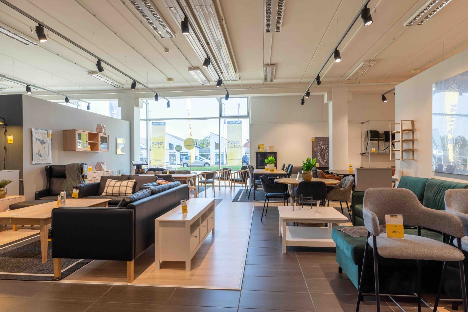 Butikslejemål med store vinduer og moderne møbler, inklusive sofaer og borde, i et komfortabelt og veludstyret butiksområde