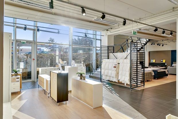 En stor butik med hvide vægge, høje vinduer og moderne møbler og indretning. Lamper og møbler er på gulvet og væggene