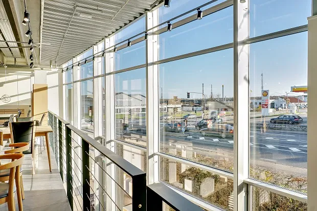 Lyst og glasfyldt kontor med udsigt til en travl vej og biler i begge retninger samt et Shell-tanksted