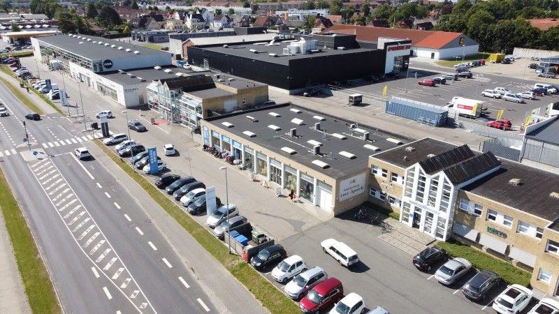 Lejemål med moderne kontorlokaler og parkeringspladser i Sønderborg. Mange biler er parkeret udenfor. Bygningen har moderne