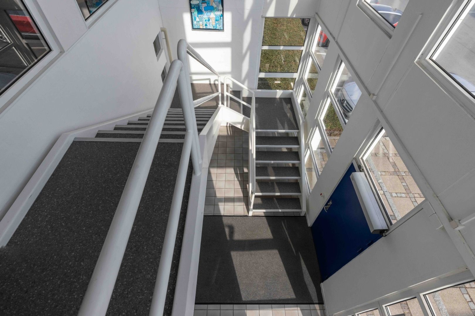 Moderne kontorlokaler med trapper, hvide vægge og lyse vinduer. Dør og gulve dækket af mønstret tæppe.