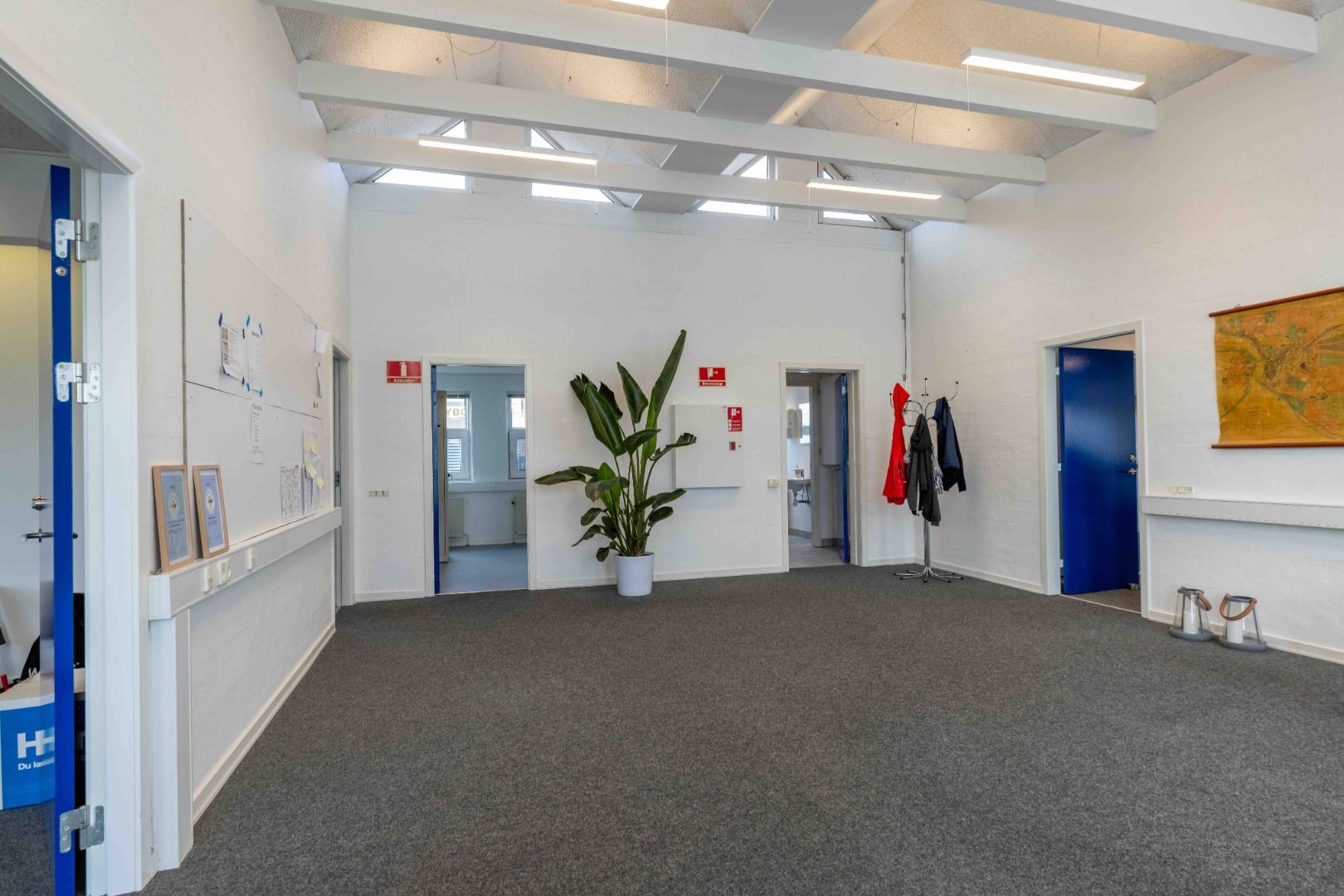 En moderne lobby med lyse loftsbjælke, lysegul gulvbelægning, indgange, tøjstativ og plante i en hvid potte