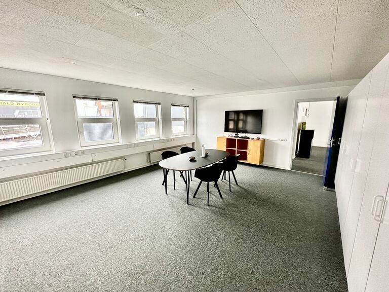 Et moderne kontor med møbler, hvide vægge og gulvtæppe, hvor der er en stor rund spisebord med fire stole