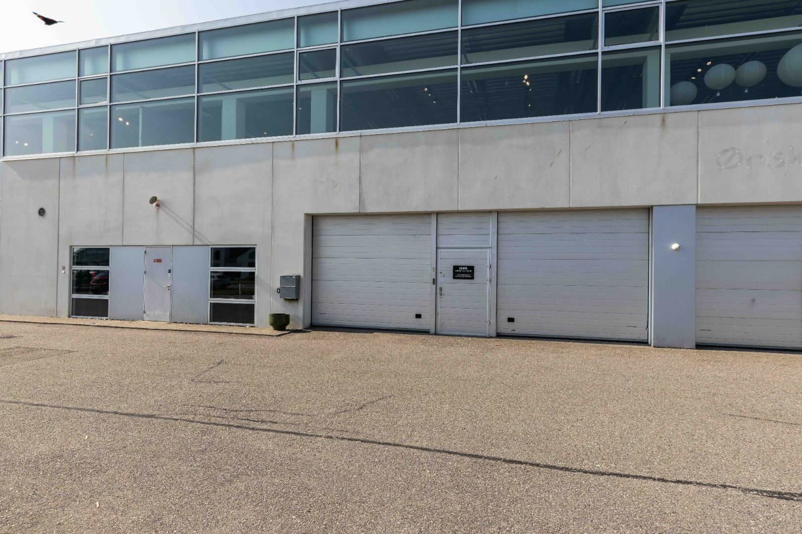 En stor, hvid bygning med glasvinduer og fire garageporte samt et skraveret ord oven på bygningen