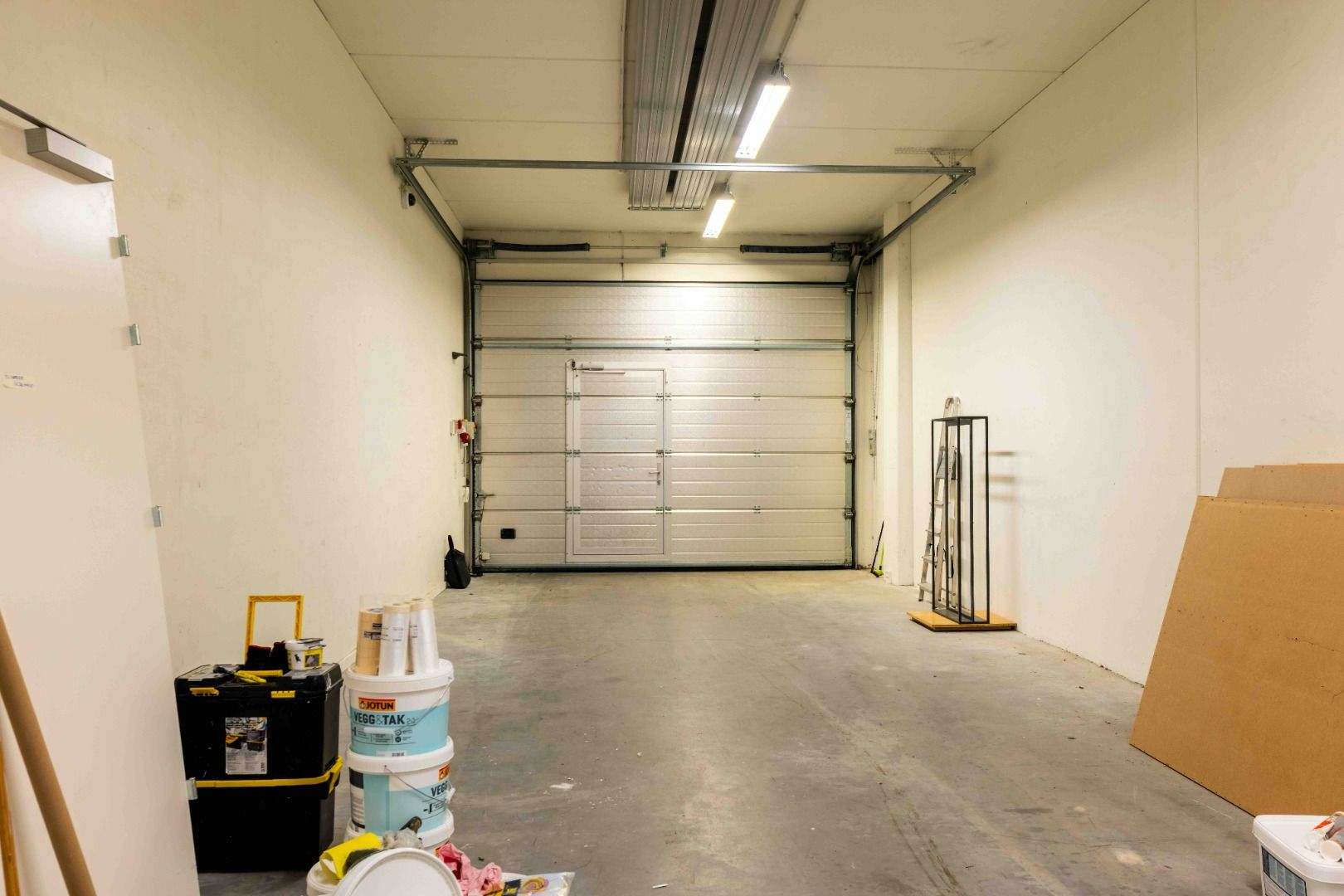 En stor garage med et lukket garagedør og flere tønde og bokse placeret på jorden i nærheden