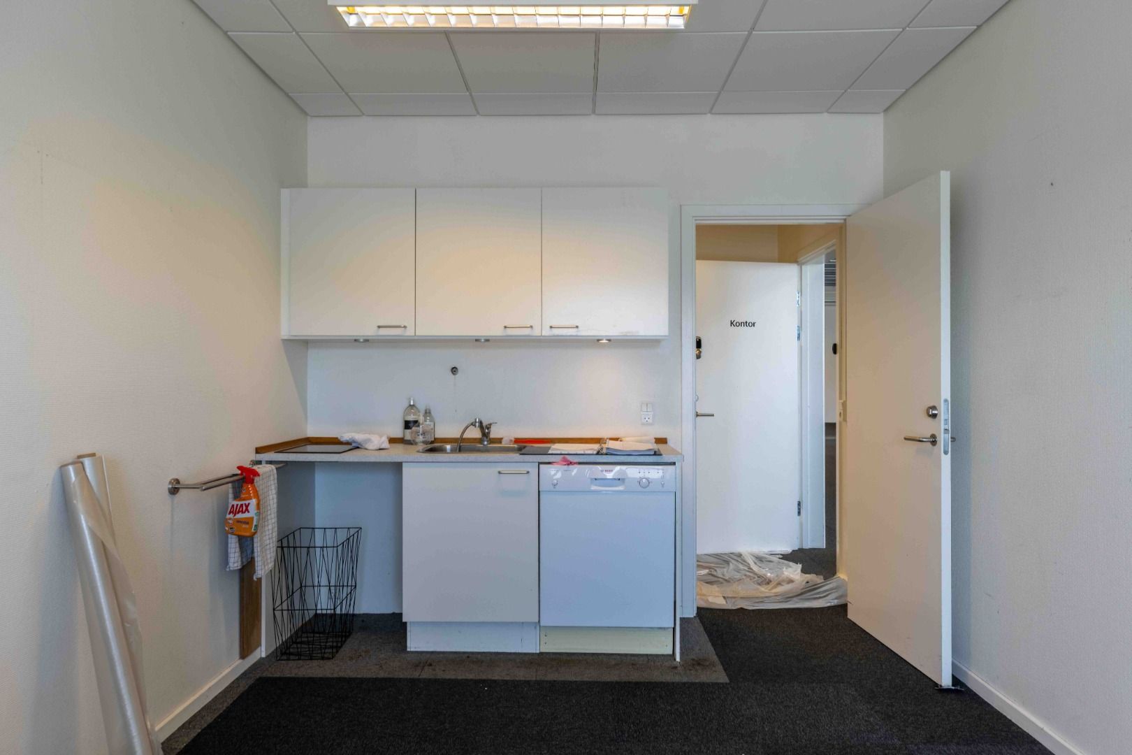 En stor, lys og ren stue med en lukket dør og en hvid køkkenhjørne med en hvid ovn og en hvid vaskemaskine i det.