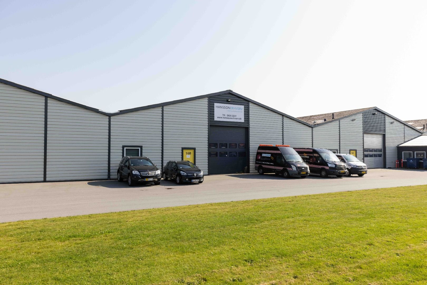 Lagerhal med mærkeplader og nummerplade og flere biler parkeret foran