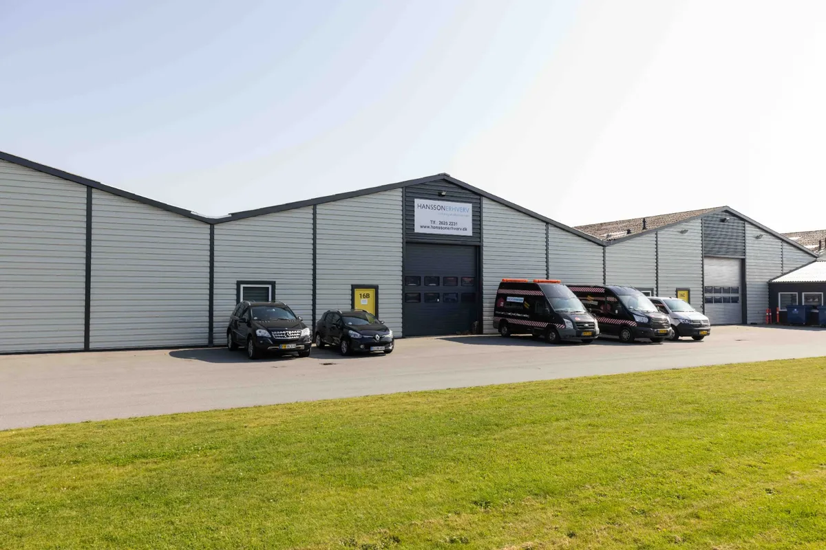 Lagerhal med mærkeplader og nummerplade og flere biler parkeret foran