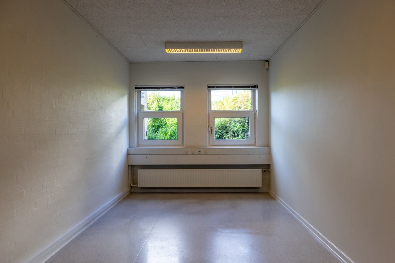 Moderne lyse lokaler med to vinduer og hvide vægge. Over vinduer er der et lys, og under er der et radiator. Loftet er hvidt