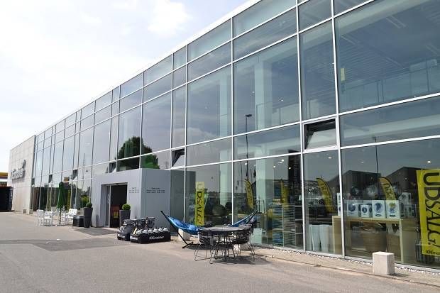 Et stort glasvinduede bygning med mange produkter udstillet på vinduet og flere bord og stole med parasoller udenfor