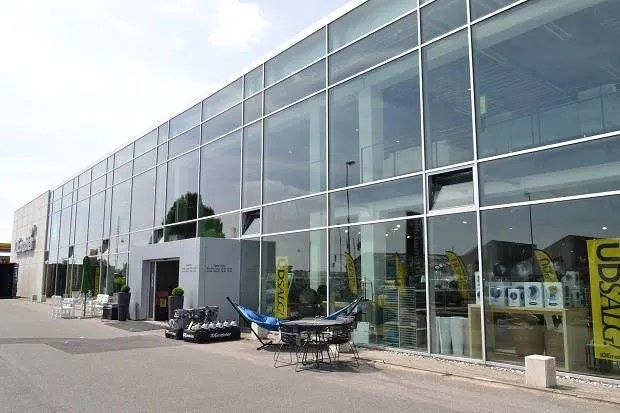 Et stort glasvinduede bygning med mange produkter udstillet på vinduet og flere bord og stole med parasoller udenfor