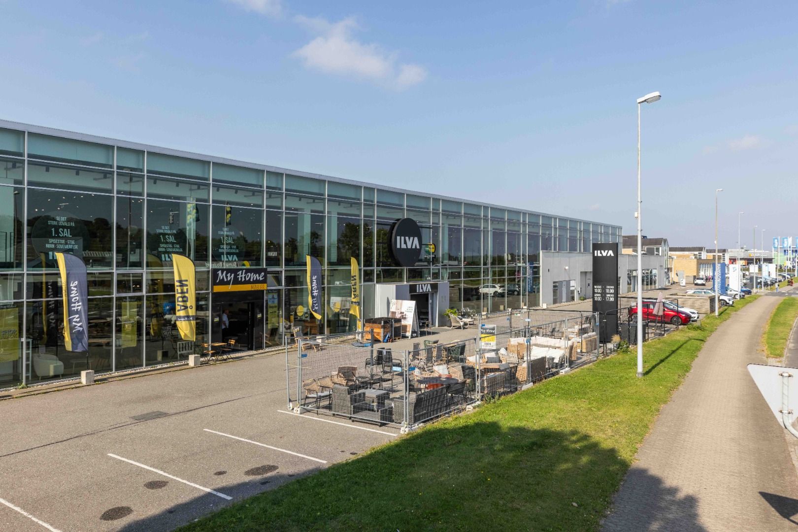 Store butikslokaler med glasvinduer, mærkenavnet ILVA, skilte med mærkenavnet ILVA, parkeringsplads og udsalg af møbler