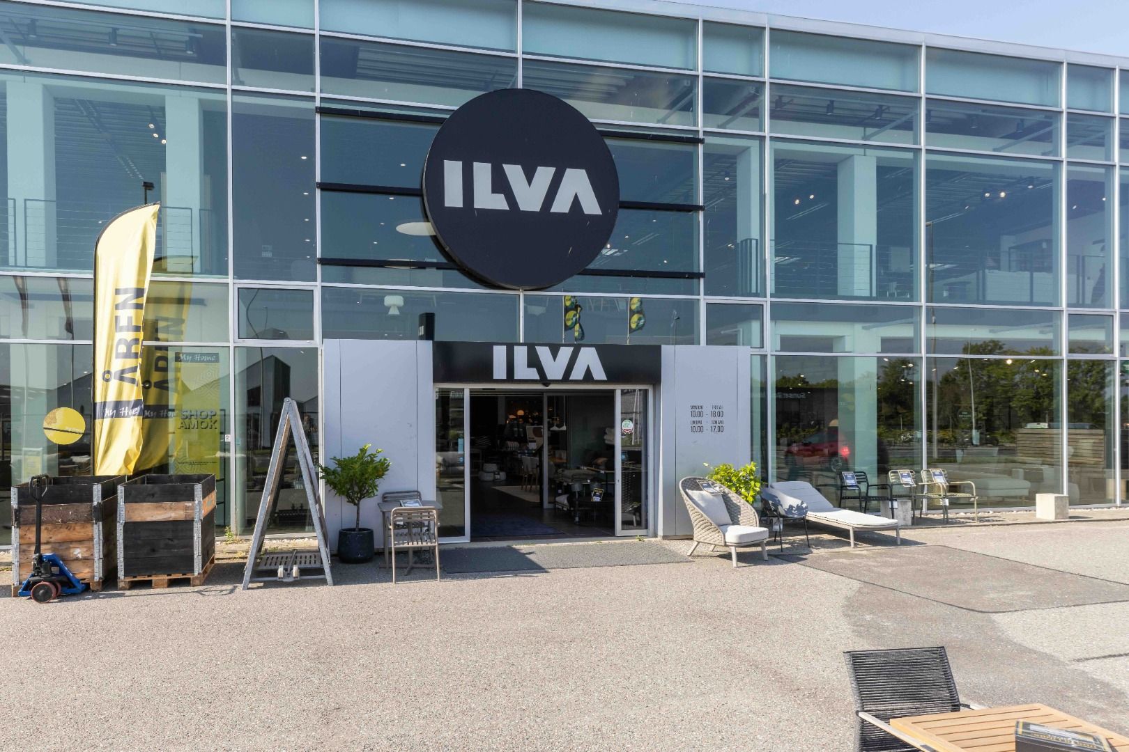En moderne ILVA butik i Sønderborg med et stort sort logo og gul banner med teksten Arend. Foran indgangen er der en plante