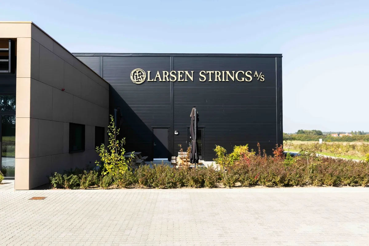 Larsen Strings' nybyggede administrations- og produktionsbygning, hvor buske og stolpe placeret foran.