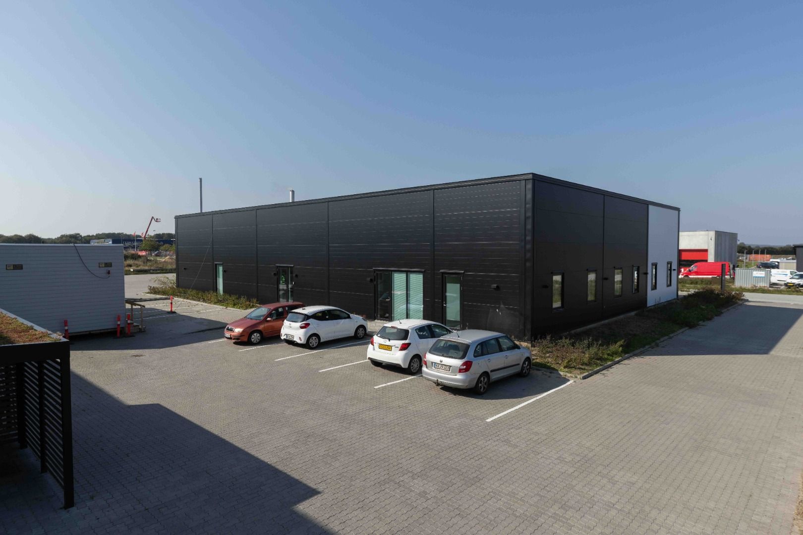 Fire biler parkeret foran et sort bygning, der sandsynligvis er en lagerbygning