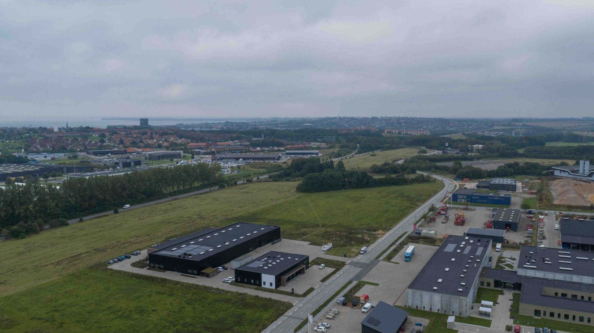 Stort produktionsanlæg med parkeringsplads og parkeret køretøj, sammen med bygninger med solceller og flere andre biler