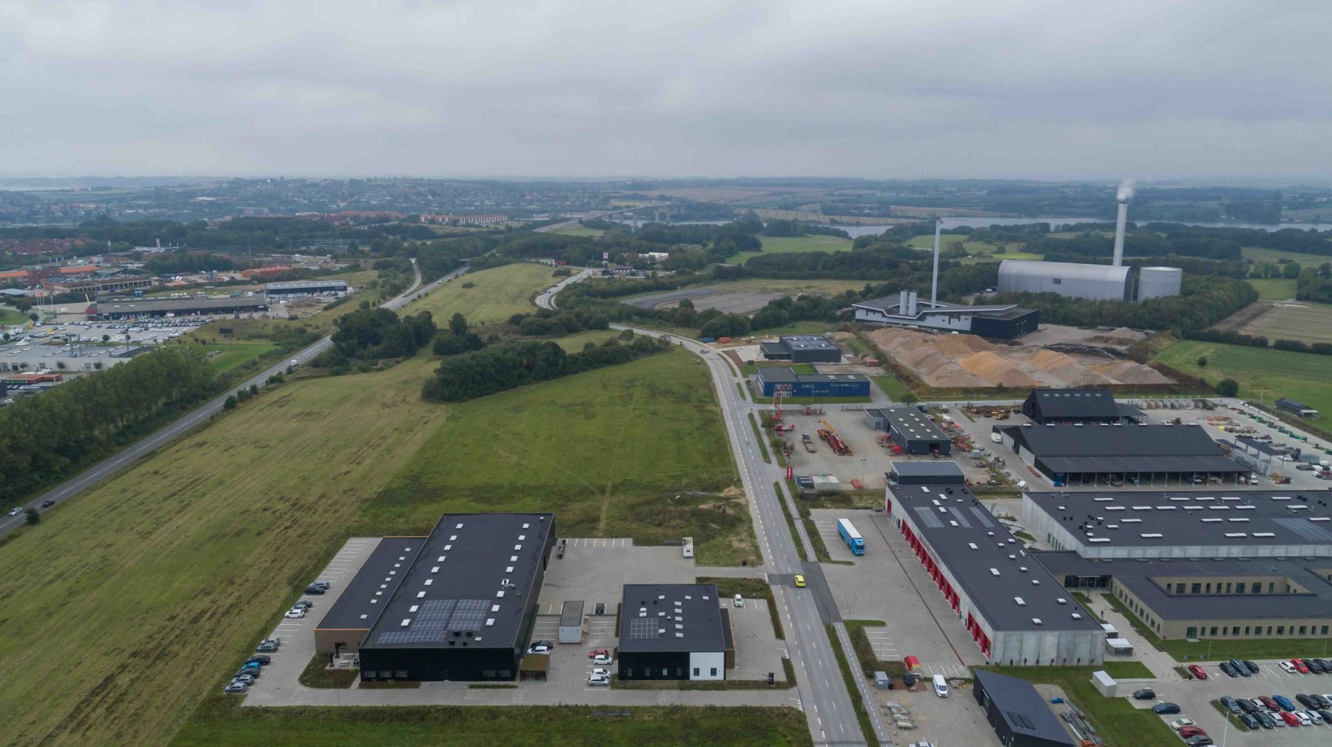 Et industriområde med store bygninger og solpaneler samt parkeringspladser og biler i baggrunden