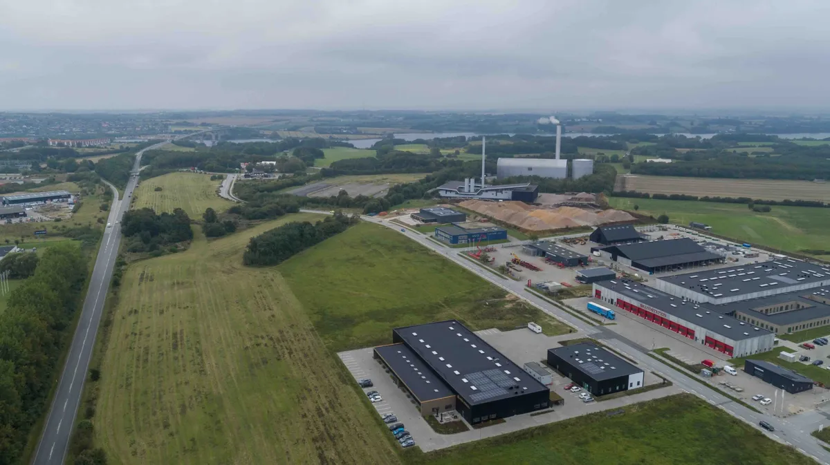 Et nybygget produktionsanlæg med moderne design og solpaneler på taget, placeret ved siden af en bred hovedvej og udstrakte