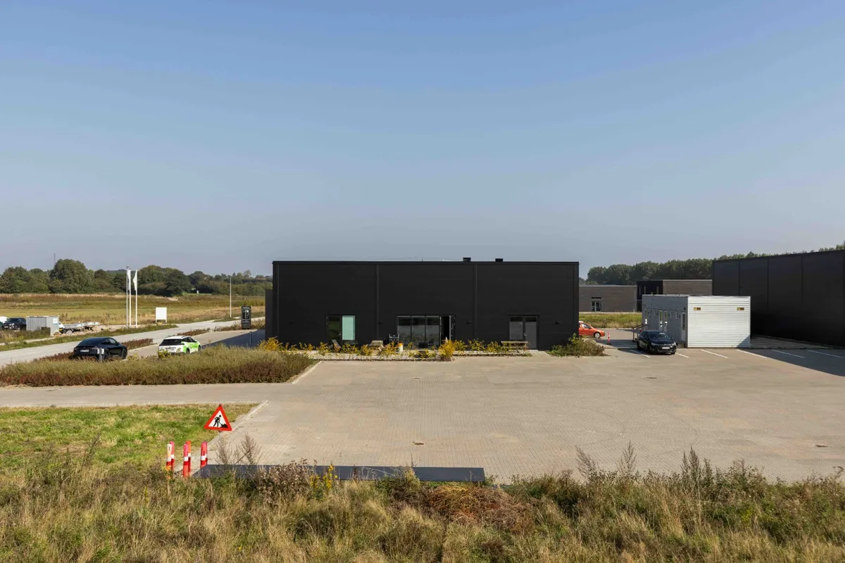 En ny bygning med store vinduer og to indgange står i en stor parkeringsplads med biler parkeret udenfor