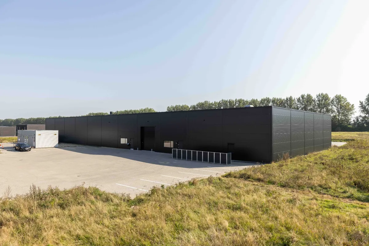 Et stort sort lagerbygning med stor parkeringsplads og græs og træer i baggrunden
