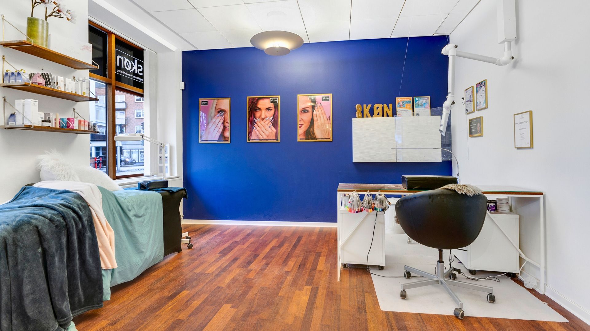 Et lyserødt vægpanel med tre billeder og en hvid sofa med puder og snor. En hvid højdeskab med højttaler og en stol med