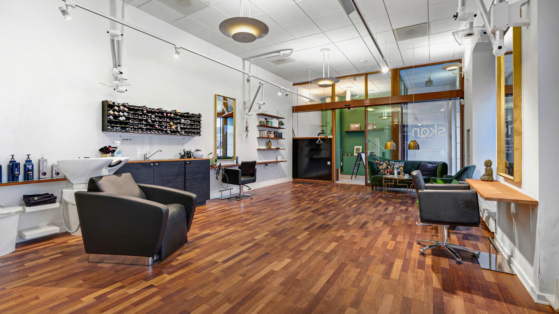 En luksuriøs frisørsalon med moderne møbler og en stor spejlvæg, der reflekterer lamperne og giver et rummeligt indtryk