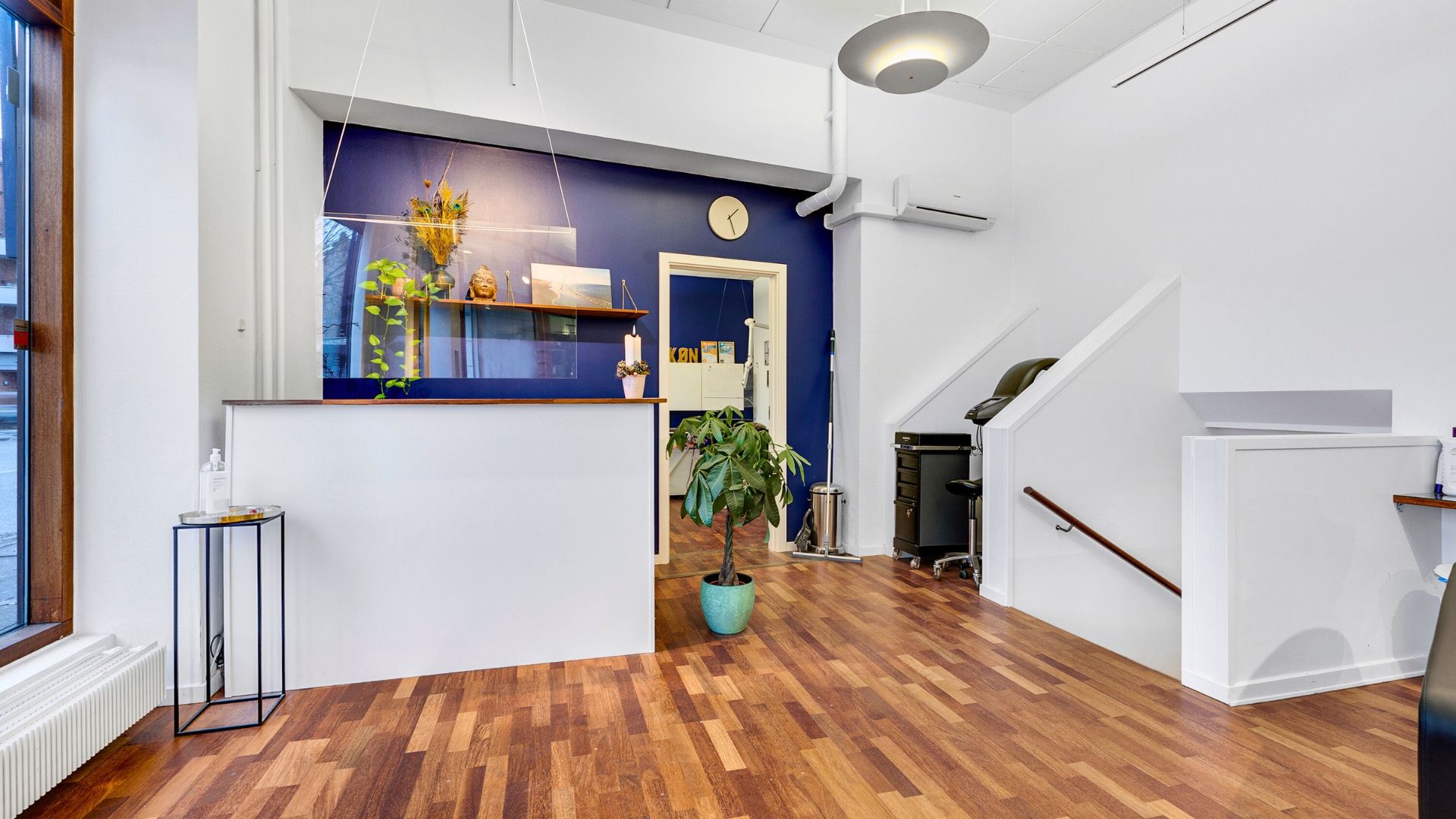 En moderne og ren lobby med en hvid væg og en brun gulv. En hvid sofa med en grøn plante og et bord med en flaske og et