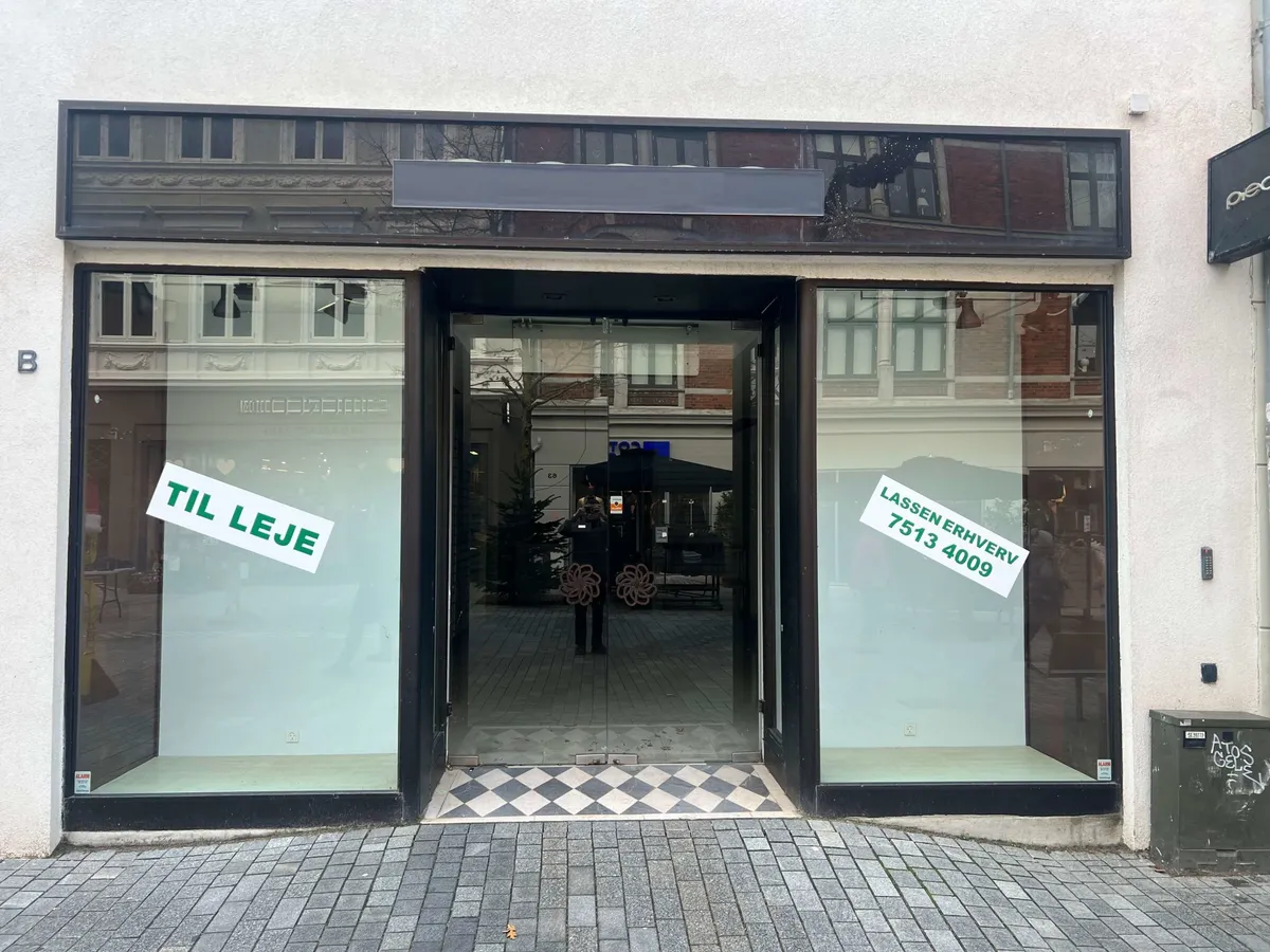 Store glasvinduer med reklame for lejligheden i København. Der står “TIL LEJE” på et glasvindue og “LASSEN ERHVVERV 7513