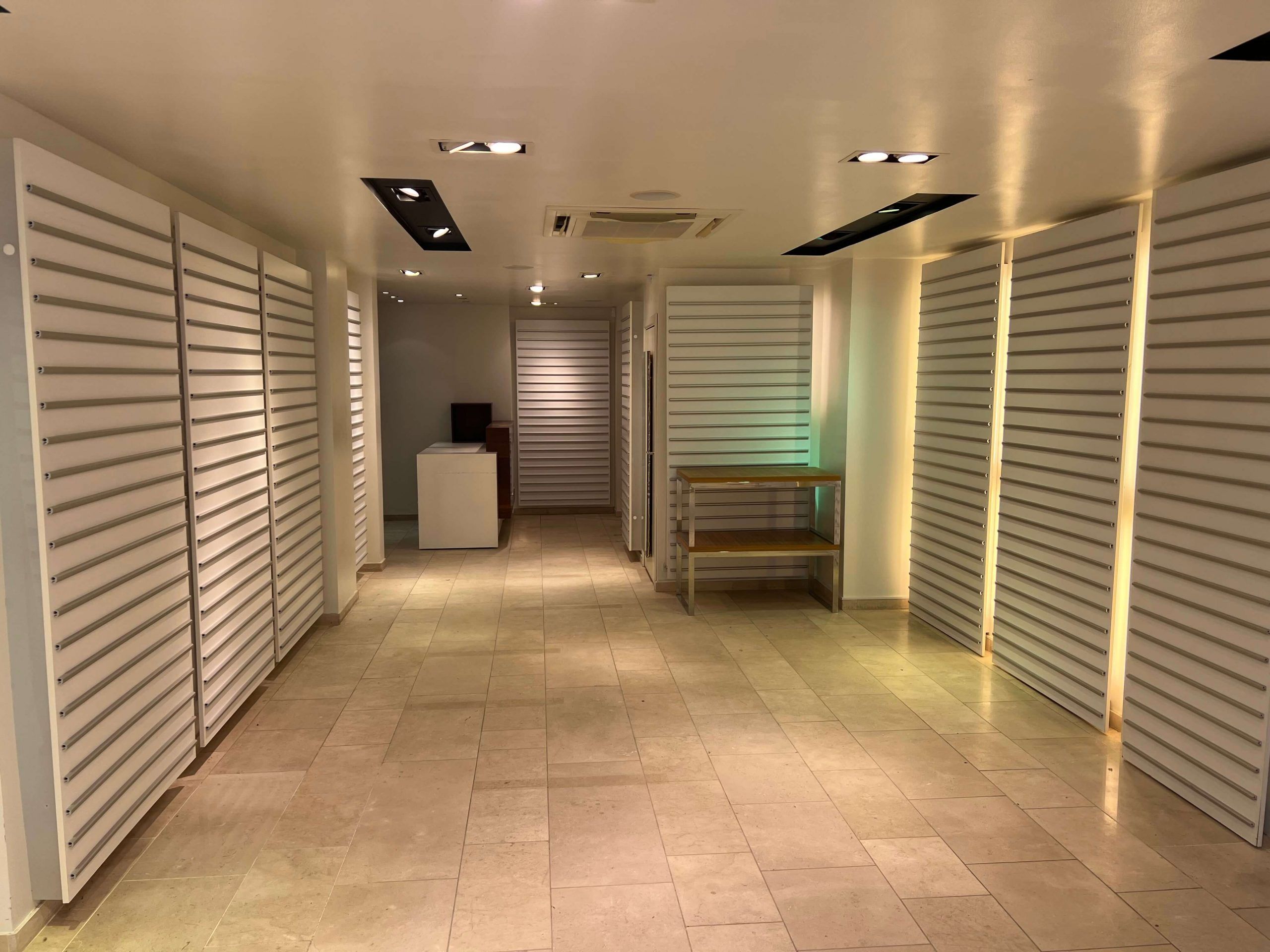 Indenfor et lyse hall med moderne hvidt loft og gulvtæppe, hvor to sæt lodrette hvide skurer er placeret mod væggene og en