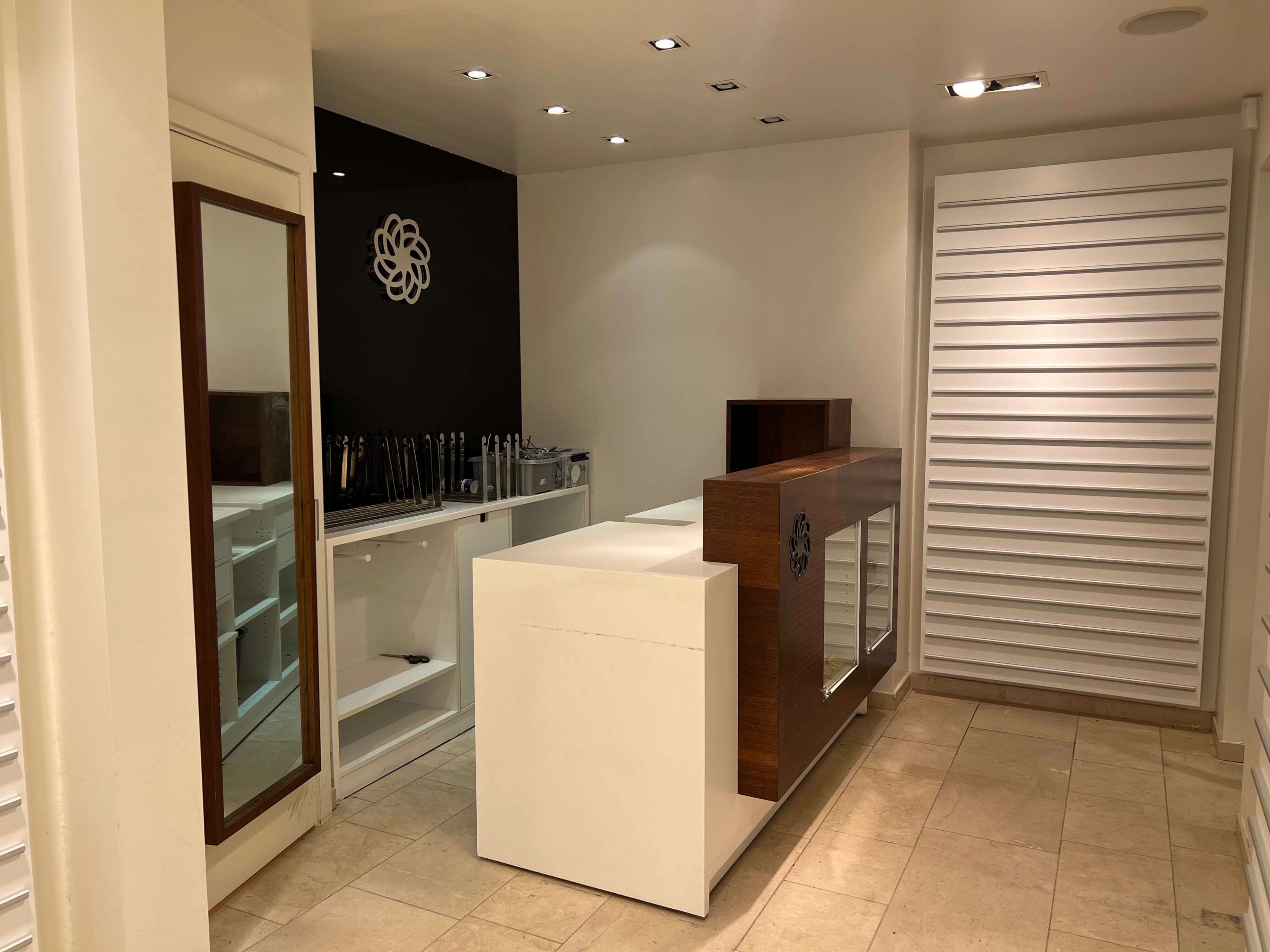 En lys stue med hvid og sort væg, lyse gulvfliser, og en høj og bred sølv og brun barre med glasdøre og en spejl på højre