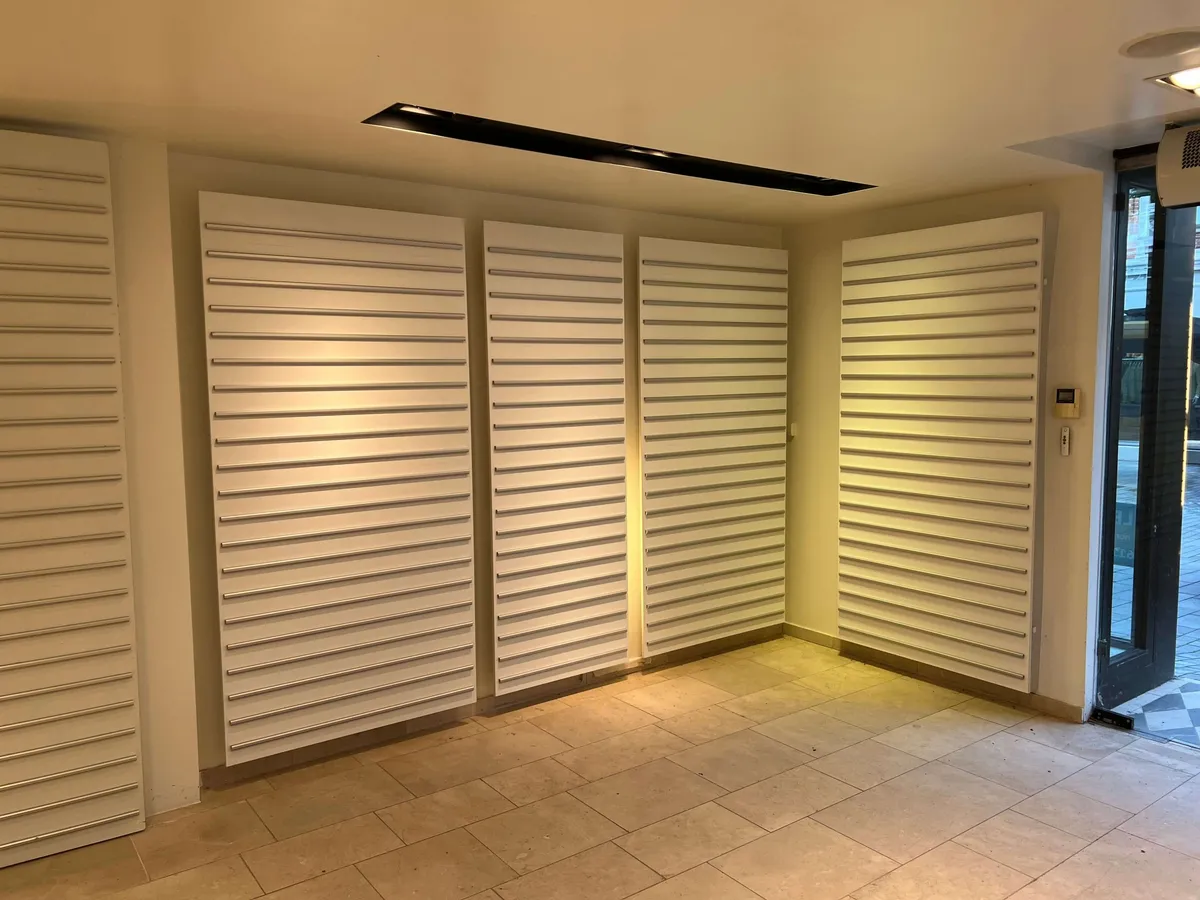 En lyse og moderne indgangsparti med hvide, slanke louver på væggen og en indbydende gulvbelægning i lysebrune fliser