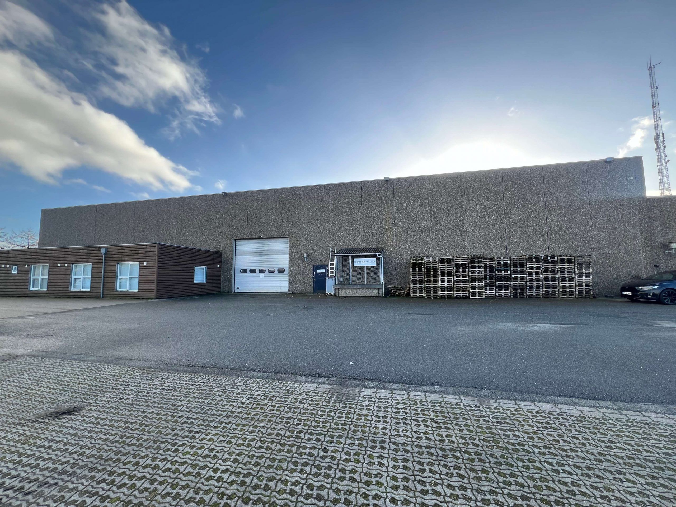 Et stort, industrielt lagerbygning med ståldør og glasvinduer og et parkeringsområde foran med et parkeret bil